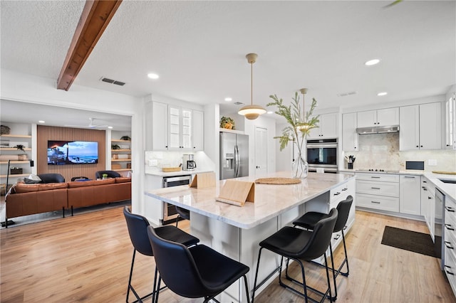 kitchen with stainless steel appliances, white cabinets, open floor plan, hanging light fixtures, and a center island