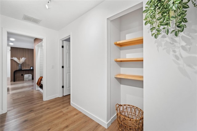 hallway featuring built in shelves, light wood-type flooring, visible vents, and baseboards