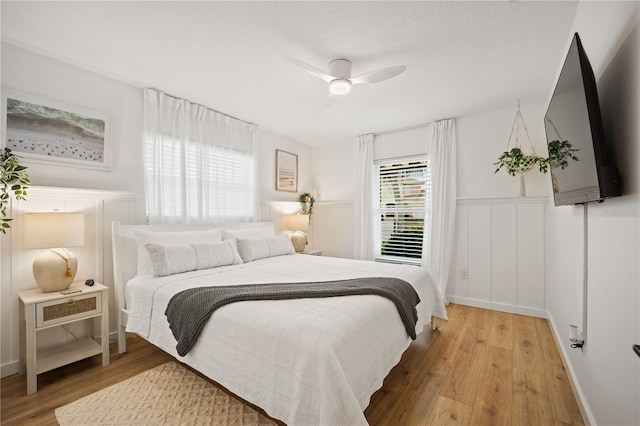 bedroom featuring a ceiling fan, wainscoting, and wood finished floors