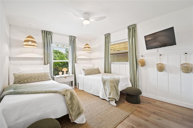 bedroom featuring a textured ceiling, a decorative wall, a wainscoted wall, wood finished floors, and a ceiling fan