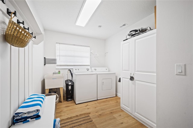 washroom featuring a textured ceiling, light wood-style flooring, laundry area, separate washer and dryer, and visible vents