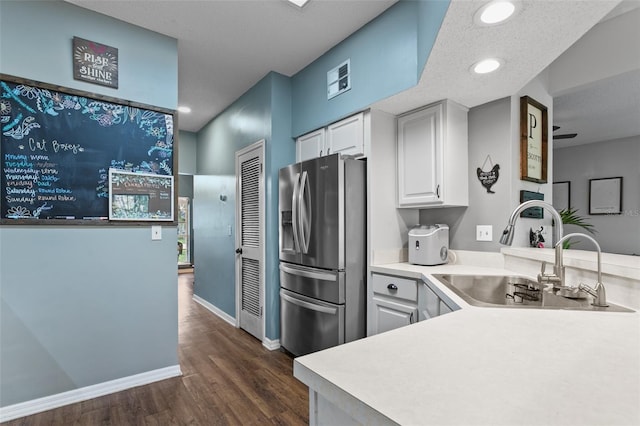 kitchen featuring stainless steel fridge, white cabinets, a peninsula, light countertops, and a sink