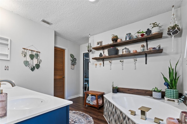 bathroom with visible vents, wood finished floors, a textured ceiling, vanity, and a bath