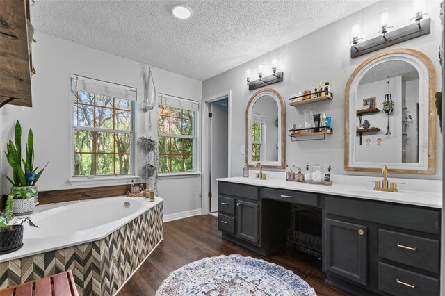 full bath featuring a textured ceiling, a garden tub, wood finished floors, a sink, and double vanity