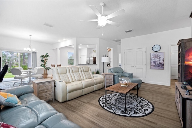 living area featuring ceiling fan with notable chandelier, wood finished floors, visible vents, and baseboards