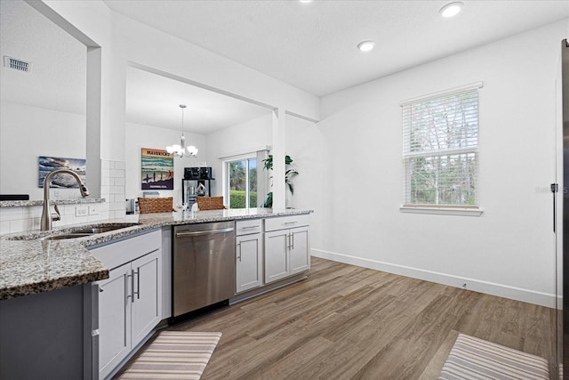 kitchen featuring a sink, visible vents, stainless steel dishwasher, light stone countertops, and light wood finished floors