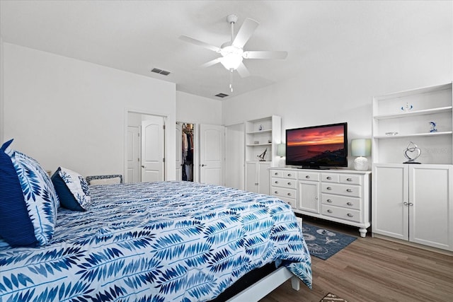 bedroom with ceiling fan, dark wood finished floors, visible vents, and a walk in closet