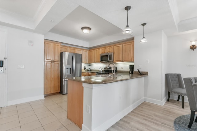 kitchen with stainless steel appliances, a peninsula, ornamental molding, a tray ceiling, and decorative light fixtures