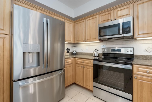 kitchen with light tile patterned floors, tasteful backsplash, dark countertops, stainless steel appliances, and light brown cabinets