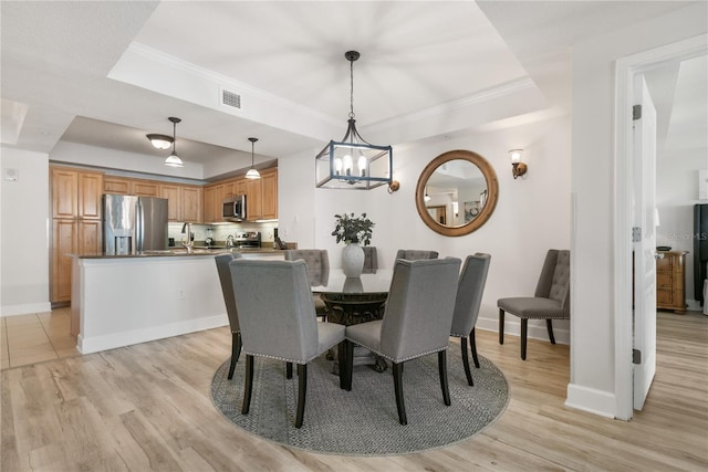 dining area featuring light wood-style flooring, visible vents, baseboards, ornamental molding, and a raised ceiling