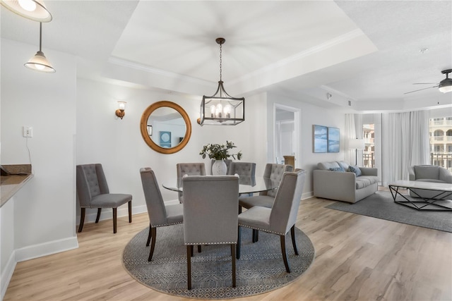 dining area with a raised ceiling, light wood-style flooring, and baseboards