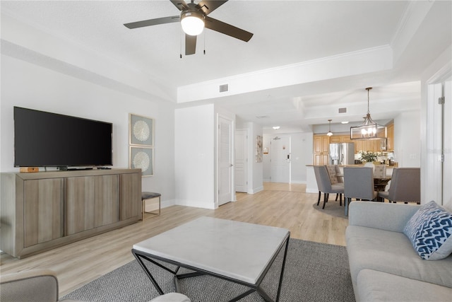 living room featuring crown molding, light wood-type flooring, a raised ceiling, and baseboards