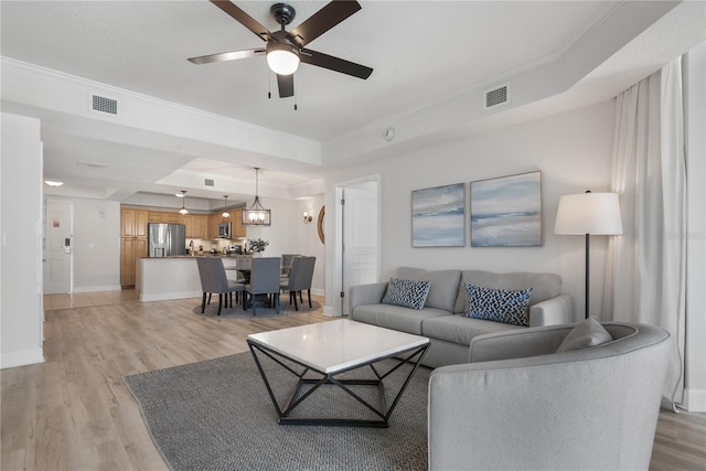 living area featuring light wood-type flooring, visible vents, crown molding, and a tray ceiling