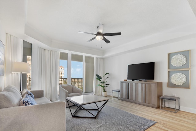 living area with ornamental molding, wood finished floors, a ceiling fan, and baseboards