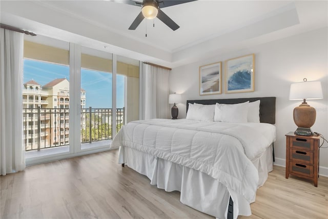 bedroom with ornamental molding, light wood-type flooring, a raised ceiling, and access to exterior