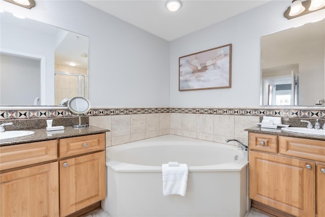 bathroom with a stall shower, two vanities, a sink, and a bath