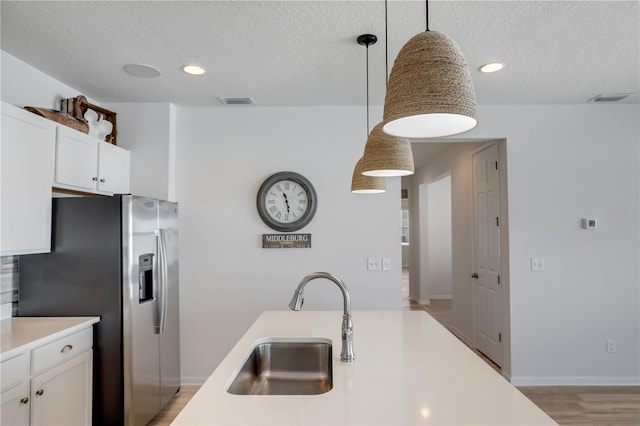 kitchen featuring stainless steel fridge, white cabinets, light countertops, pendant lighting, and a sink