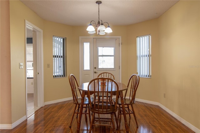 dining space featuring a textured ceiling, dark wood-type flooring, an inviting chandelier, and baseboards