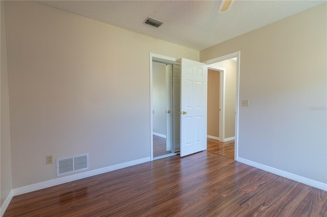 unfurnished bedroom featuring dark wood-style floors, visible vents, a textured ceiling, and baseboards