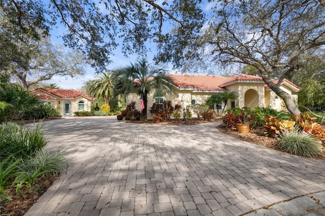 mediterranean / spanish-style house featuring a tiled roof, decorative driveway, and stucco siding