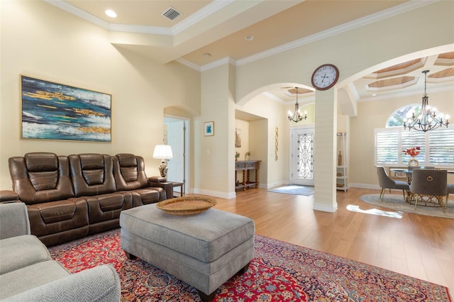 living area featuring arched walkways, a notable chandelier, wood finished floors, visible vents, and ornamental molding