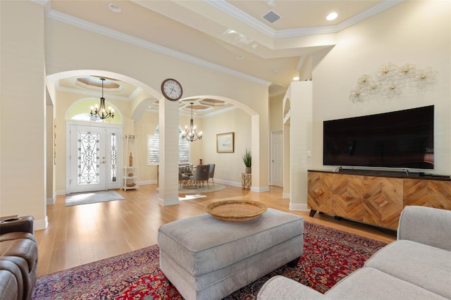 living area with visible vents, arched walkways, ornamental molding, wood finished floors, and a chandelier