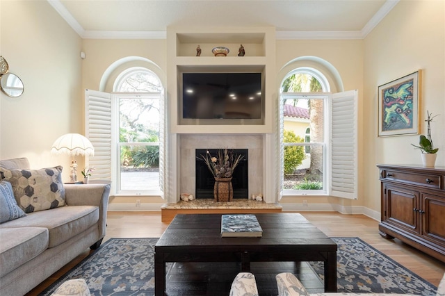 living area featuring a healthy amount of sunlight, a fireplace, ornamental molding, and wood finished floors