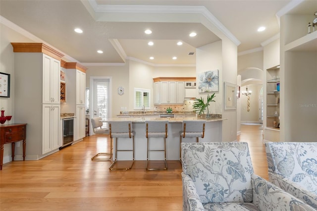 kitchen with light wood finished floors, beverage cooler, arched walkways, a kitchen breakfast bar, and a peninsula