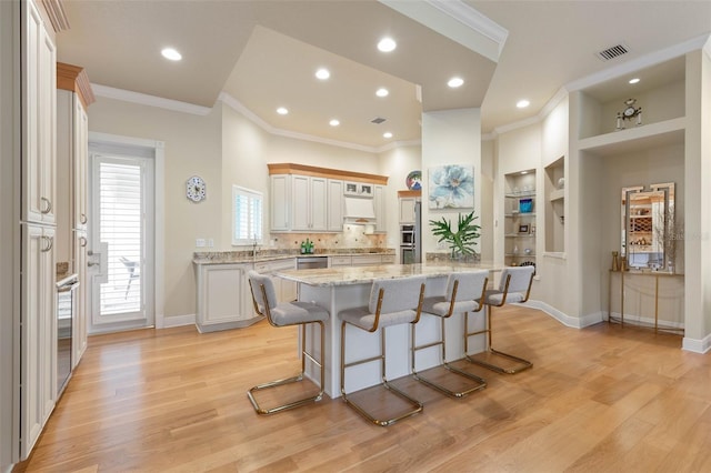 kitchen with light stone counters, visible vents, light wood-style flooring, ornamental molding, and a kitchen breakfast bar