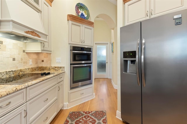 kitchen featuring stainless steel appliances, light wood-type flooring, premium range hood, and backsplash