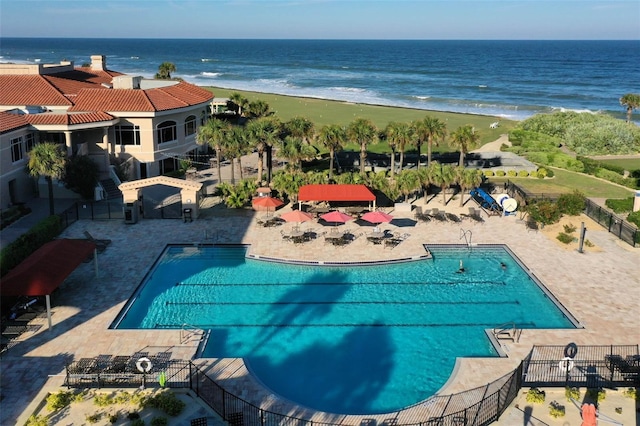 pool with a patio area, a water view, fence, and a beach view