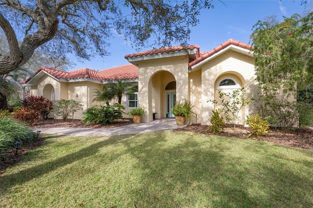 mediterranean / spanish-style house featuring a tile roof, a front yard, and stucco siding