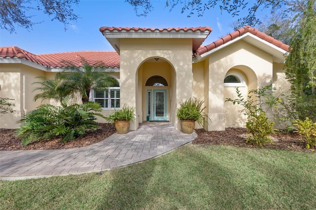 doorway to property with a tile roof, a yard, and stucco siding