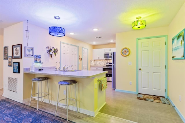 kitchen featuring visible vents, appliances with stainless steel finishes, white cabinetry, a peninsula, and a kitchen breakfast bar