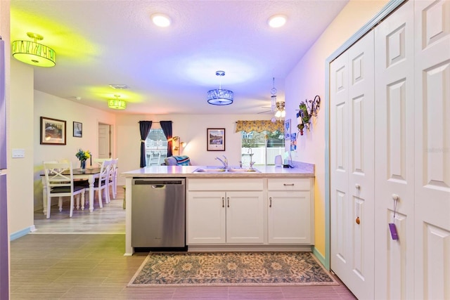 kitchen featuring white cabinets, a peninsula, a healthy amount of sunlight, stainless steel dishwasher, and a sink