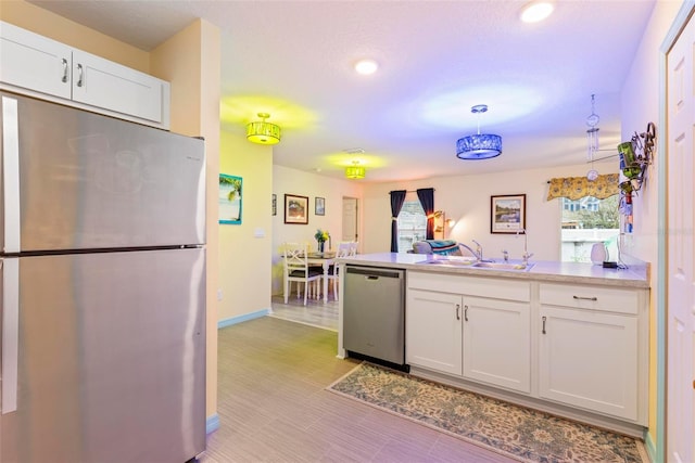 kitchen with light countertops, appliances with stainless steel finishes, white cabinets, a sink, and a peninsula