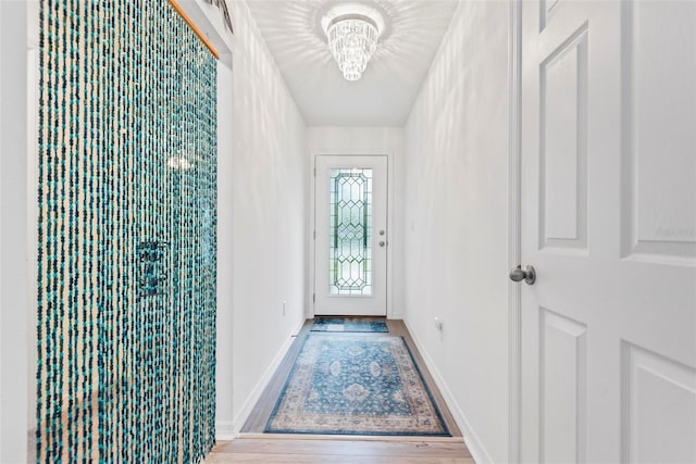 doorway featuring baseboards, a chandelier, and wood finished floors