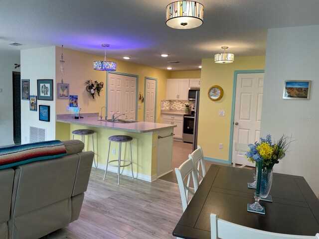 8 Smoke Tree Pl, Palm Coast, FL 32164 - kitchen featuring a peninsula, a kitchen bar, a sink, white cabinetry, and light wood-style flooring