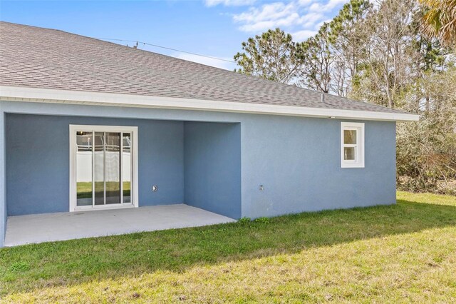 back of house featuring stucco siding, roof with shingles, a patio, and a lawn