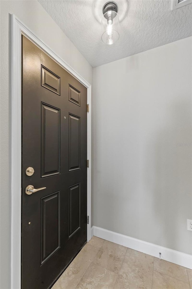 entrance foyer with a textured ceiling, light tile patterned floors, and baseboards