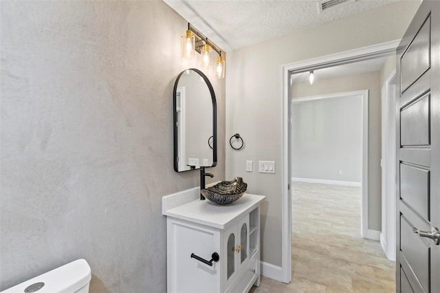 half bathroom featuring visible vents, toilet, a textured ceiling, vanity, and baseboards