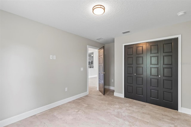 unfurnished bedroom featuring a textured ceiling, a closet, visible vents, and baseboards