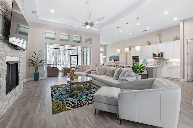 living room with light wood-style flooring, a high ceiling, a fireplace, visible vents, and a tray ceiling