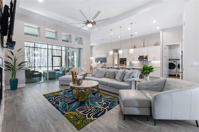 living area with a ceiling fan, washing machine and dryer, a high ceiling, and wood finished floors