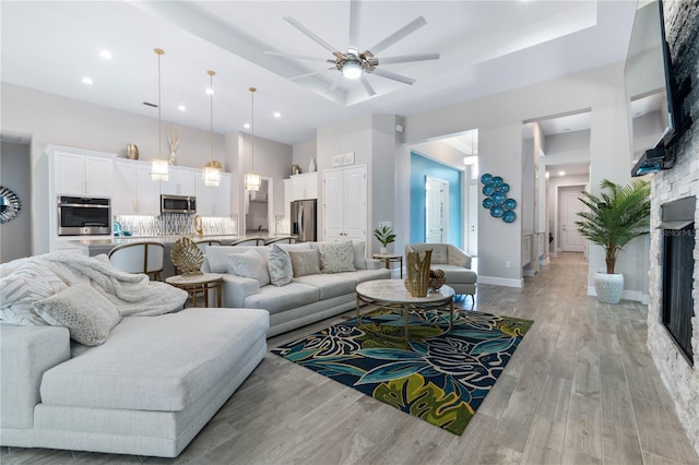 living area featuring light wood-type flooring, a tray ceiling, baseboards, and a ceiling fan