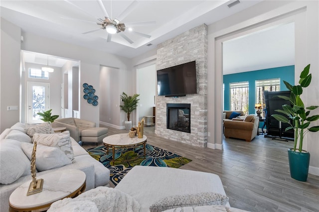 living room featuring visible vents, ceiling fan, a stone fireplace, wood finished floors, and baseboards