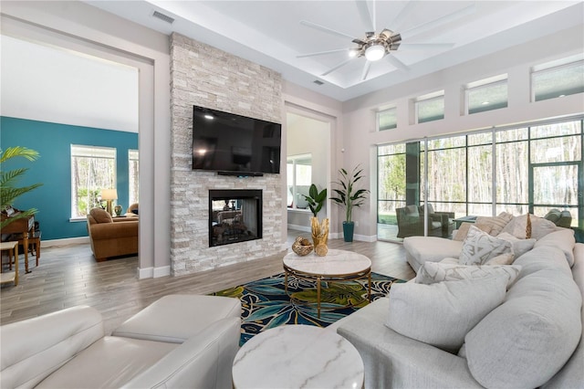 living room featuring a stone fireplace, wood finished floors, visible vents, and baseboards