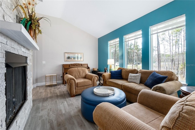 living room with vaulted ceiling, a stone fireplace, wood finished floors, and baseboards