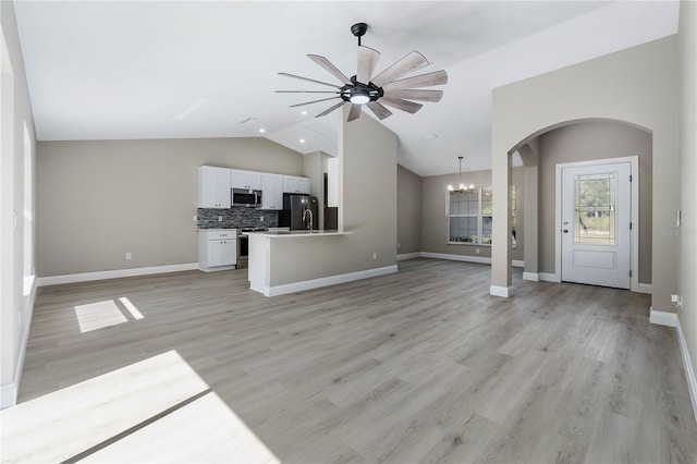 unfurnished living room featuring lofted ceiling, arched walkways, light wood-style flooring, ceiling fan with notable chandelier, and baseboards