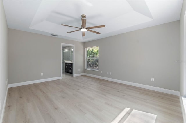 unfurnished room featuring a tray ceiling, light wood-style floors, visible vents, and baseboards